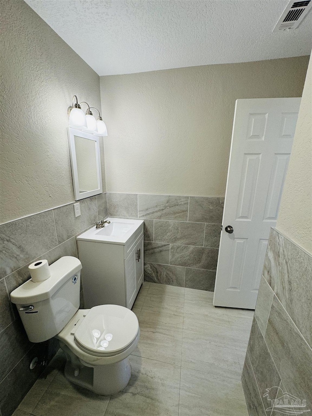 bathroom with vanity, tile patterned floors, toilet, a textured ceiling, and tile walls