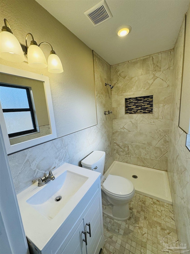 bathroom with vanity, toilet, tile walls, tiled shower, and tasteful backsplash