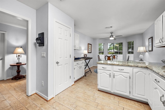 kitchen with light hardwood / wood-style floors, white cabinetry, kitchen peninsula, light stone countertops, and ceiling fan