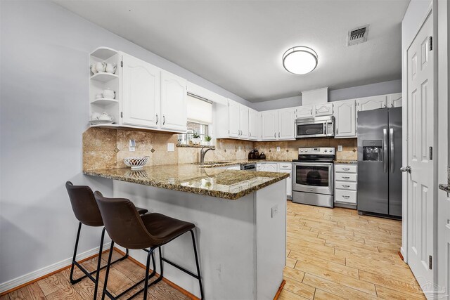 kitchen featuring stainless steel appliances, dark stone countertops, kitchen peninsula, and white cabinets