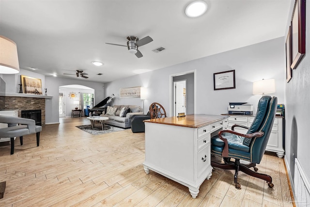 office space featuring ceiling fan, a fireplace, and light hardwood / wood-style floors