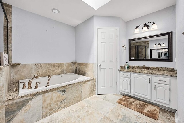 bathroom featuring a skylight, a relaxing tiled tub, and vanity