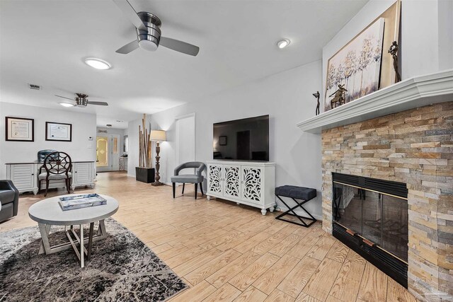 living room featuring ceiling fan, a stone fireplace, and light wood-type flooring