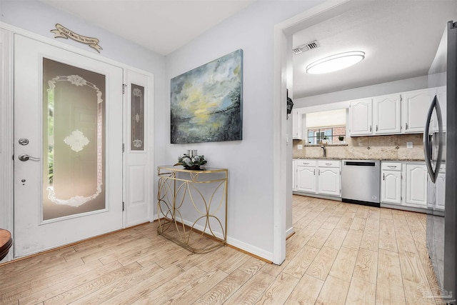 kitchen featuring white cabinets, light hardwood / wood-style flooring, appliances with stainless steel finishes, light stone countertops, and decorative backsplash