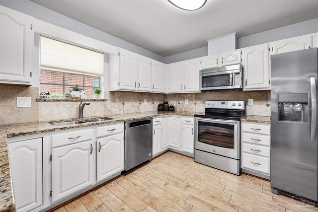 kitchen featuring appliances with stainless steel finishes, light hardwood / wood-style floors, light stone counters, white cabinets, and sink