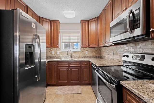 kitchen with sink, light stone counters, light tile patterned floors, stainless steel appliances, and backsplash