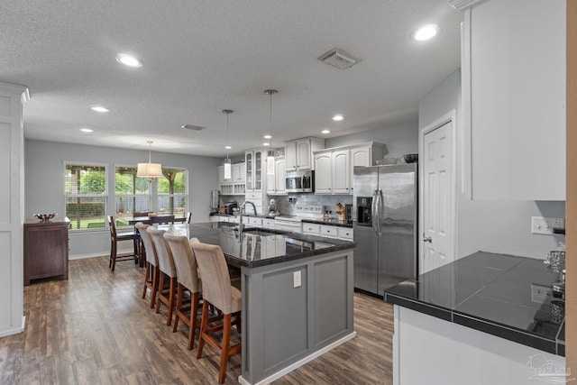 2215 Seascale Ct, Navarre, FL 32566 - kitchen with stainless steel appliances, dark countertops, a sink, a breakfast bar, and dark wood-style floors