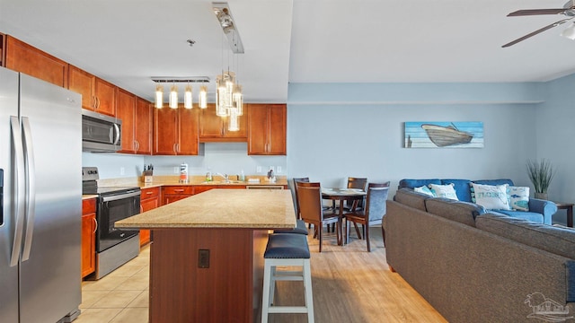 kitchen with a center island, a breakfast bar area, ceiling fan with notable chandelier, light hardwood / wood-style flooring, and stainless steel appliances