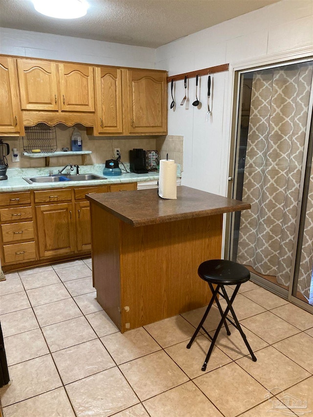 kitchen featuring light tile patterned floors, a textured ceiling, a center island, sink, and a kitchen bar