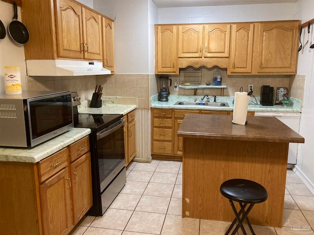 kitchen featuring light tile patterned flooring, a kitchen island, appliances with stainless steel finishes, decorative backsplash, and sink