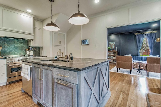 kitchen with sink, light hardwood / wood-style floors, pendant lighting, a kitchen island with sink, and appliances with stainless steel finishes