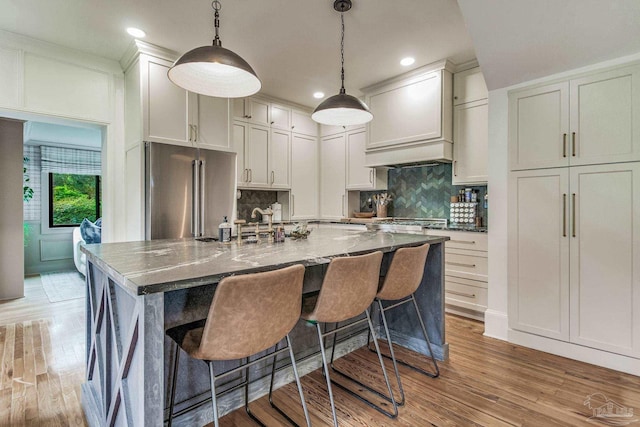 kitchen with high end refrigerator, light wood-type flooring, dark stone counters, decorative light fixtures, and a large island