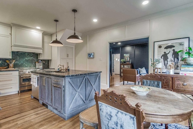 kitchen featuring sink, hanging light fixtures, high end stove, light wood-type flooring, and an island with sink