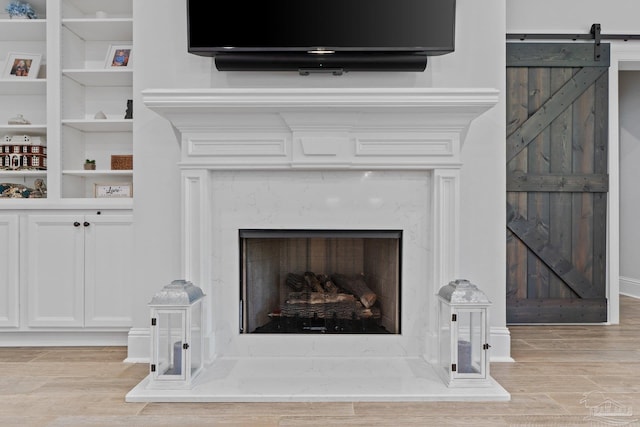 details with a fireplace, wood-type flooring, a barn door, and built in shelves