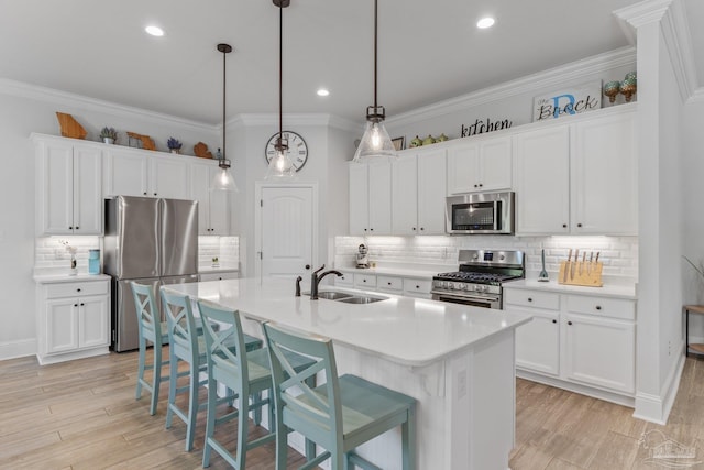 kitchen with hanging light fixtures, stainless steel appliances, a center island with sink, sink, and white cabinets