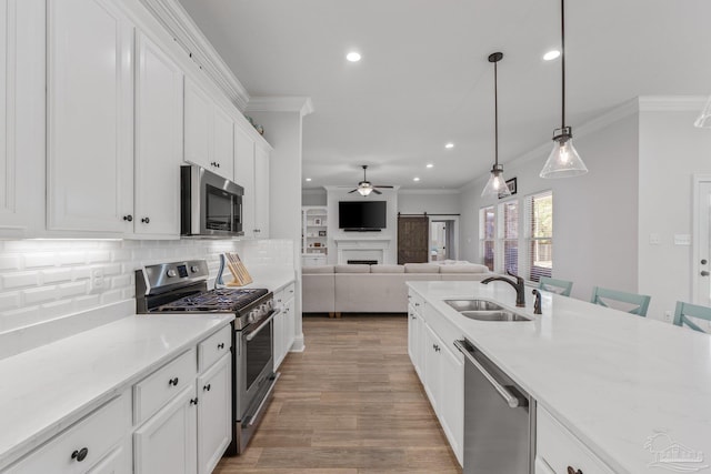 kitchen with appliances with stainless steel finishes, sink, a barn door, hanging light fixtures, and white cabinetry