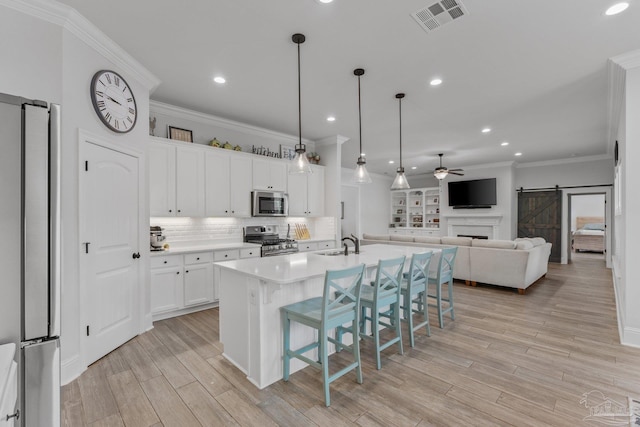 kitchen featuring white cabinets, an island with sink, appliances with stainless steel finishes, a barn door, and light wood-type flooring