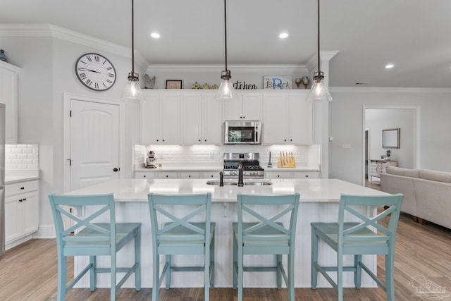 kitchen with white cabinetry, light hardwood / wood-style floors, stainless steel appliances, pendant lighting, and a kitchen island with sink