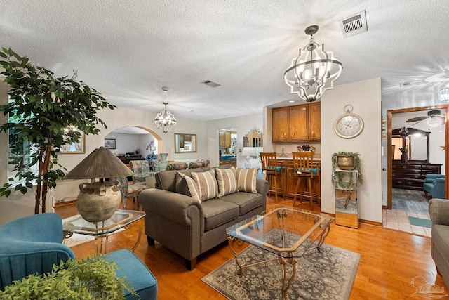 living room featuring ceiling fan with notable chandelier, light hardwood / wood-style floors, and a textured ceiling