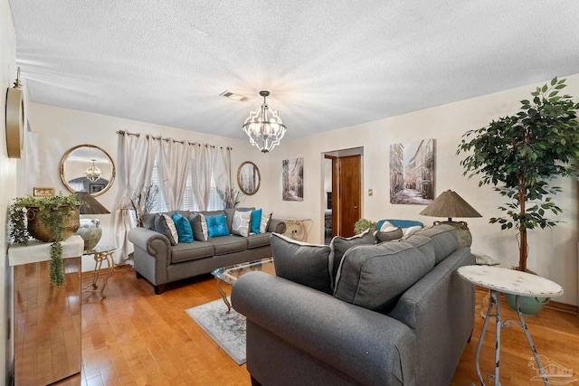 living room with a textured ceiling, light hardwood / wood-style flooring, and an inviting chandelier