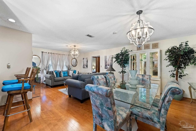 dining space featuring a notable chandelier, a healthy amount of sunlight, wood-type flooring, and a textured ceiling