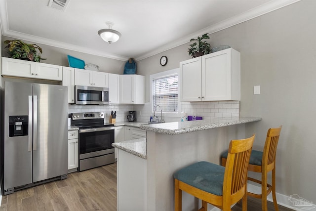 kitchen featuring a breakfast bar area, appliances with stainless steel finishes, ornamental molding, white cabinetry, and a sink