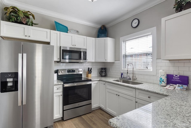 kitchen with crown molding, appliances with stainless steel finishes, white cabinetry, a sink, and light wood-type flooring