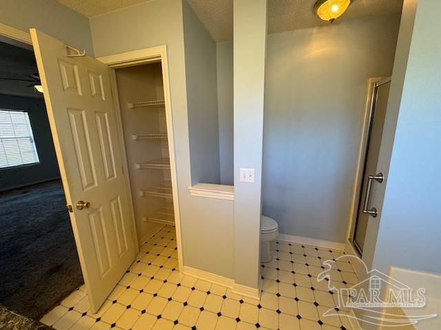 bathroom with ceiling fan, a shower with door, a textured ceiling, and toilet