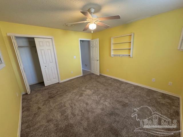 unfurnished bedroom featuring ceiling fan, dark carpet, a textured ceiling, and a closet