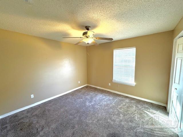 empty room featuring ceiling fan, dark carpet, and a textured ceiling