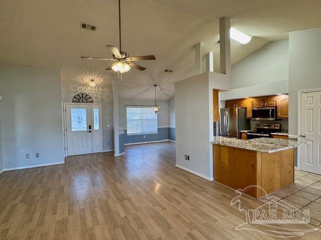 kitchen featuring ceiling fan, light stone counters, high vaulted ceiling, light hardwood / wood-style floors, and appliances with stainless steel finishes