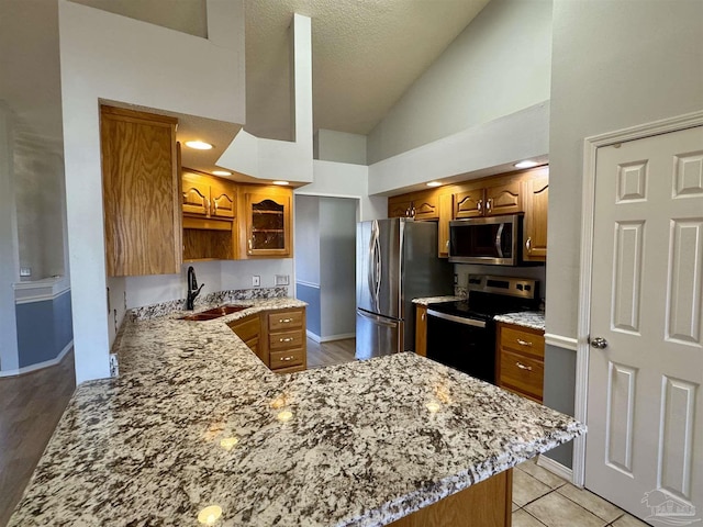 kitchen featuring a sink, brown cabinets, stainless steel appliances, a peninsula, and light stone counters
