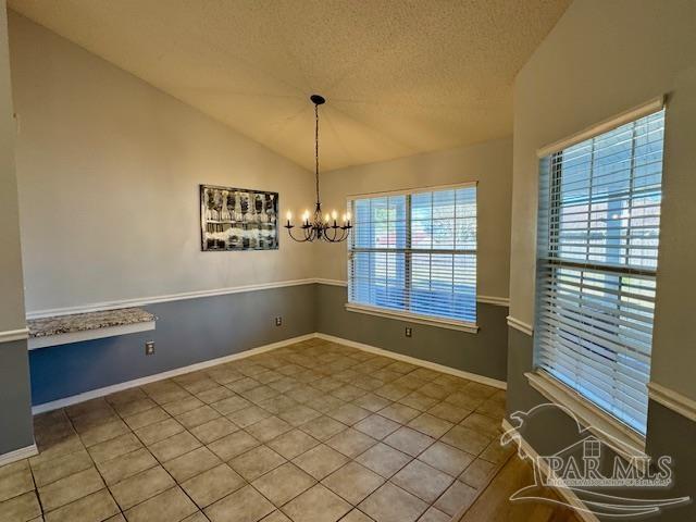 unfurnished dining area with tile patterned floors, a textured ceiling, vaulted ceiling, and a notable chandelier