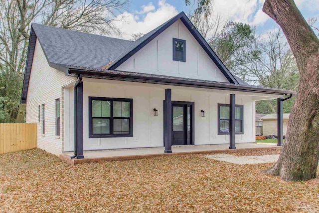 modern inspired farmhouse featuring brick siding, covered porch, roof with shingles, and fence