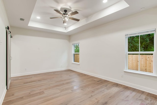 unfurnished room with ceiling fan, baseboards, light wood-type flooring, and a tray ceiling