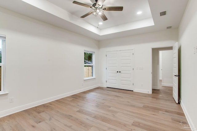 spare room featuring a tray ceiling, baseboards, light wood-style floors, and visible vents