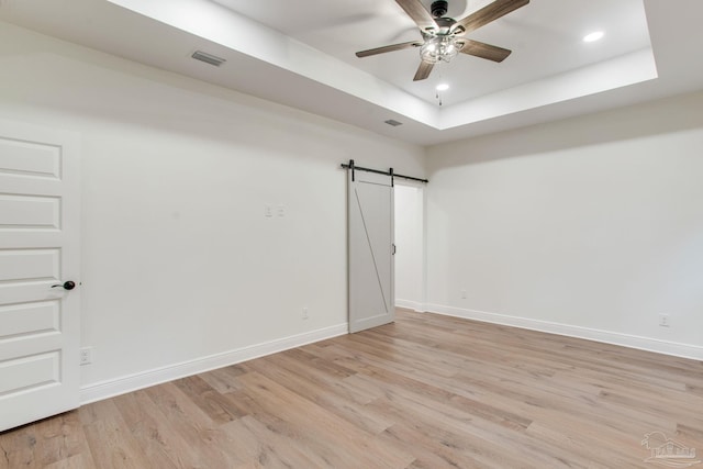 spare room featuring visible vents, light wood-type flooring, a tray ceiling, a barn door, and baseboards