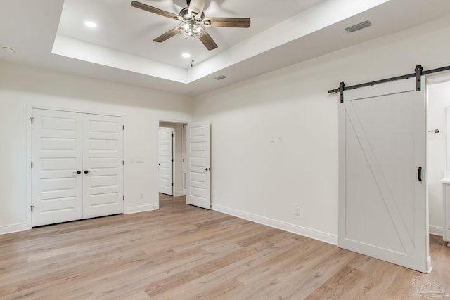 unfurnished bedroom with a barn door, visible vents, light wood-style flooring, and a tray ceiling