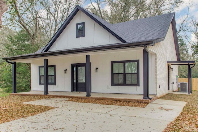 modern farmhouse with central AC unit, brick siding, a porch, and a shingled roof