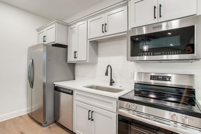 kitchen with light wood finished floors, a sink, decorative backsplash, light countertops, and stainless steel appliances