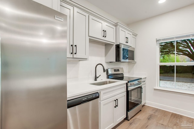 kitchen with light wood-style flooring, a sink, stainless steel appliances, light countertops, and backsplash