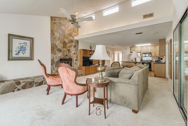 living room with a fireplace, light colored carpet, visible vents, a high ceiling, and ceiling fan