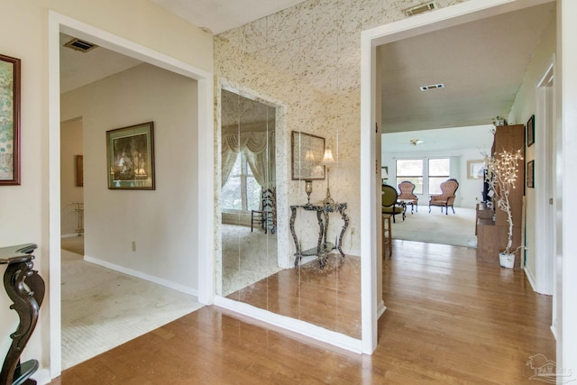 hall with baseboards, visible vents, and wood finished floors