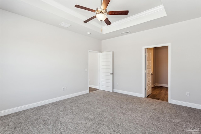 unfurnished bedroom with dark colored carpet, connected bathroom, ceiling fan, and a tray ceiling