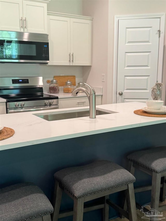 kitchen with stainless steel appliances, sink, a breakfast bar area, and white cabinets