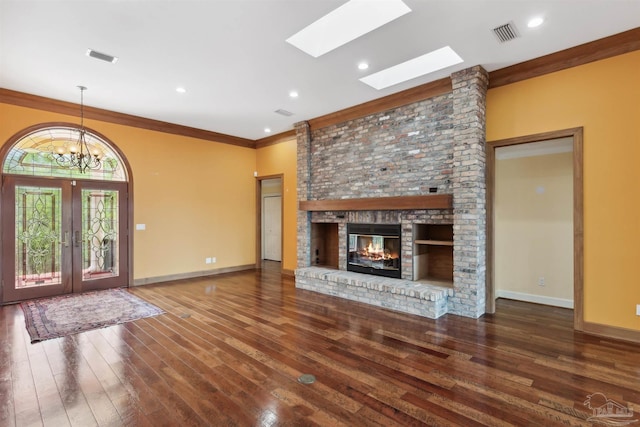 unfurnished living room with ornamental molding, a brick fireplace, dark wood-type flooring, an inviting chandelier, and french doors