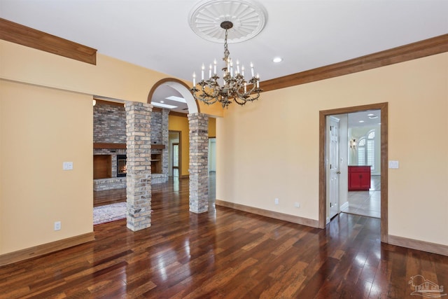 spare room featuring ornate columns, crown molding, dark wood-type flooring, and a fireplace