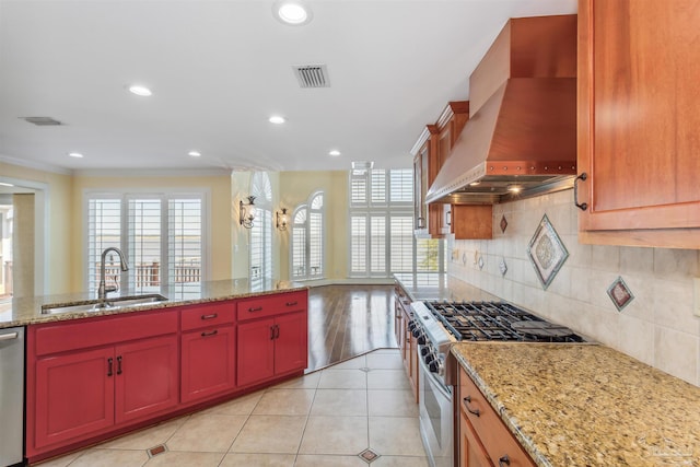 kitchen featuring wall chimney exhaust hood, sink, stainless steel appliances, light stone countertops, and decorative backsplash