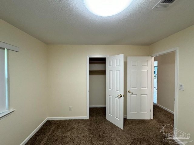 unfurnished bedroom with a textured ceiling, dark colored carpet, and a closet