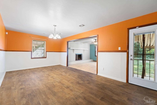 unfurnished room with hardwood / wood-style flooring, plenty of natural light, ceiling fan with notable chandelier, and a brick fireplace